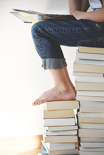 Barefoot Person Sitting On Stack Of Books Reading Magazine