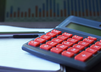 Close-up of red calculator on notebook with blurred financial charts