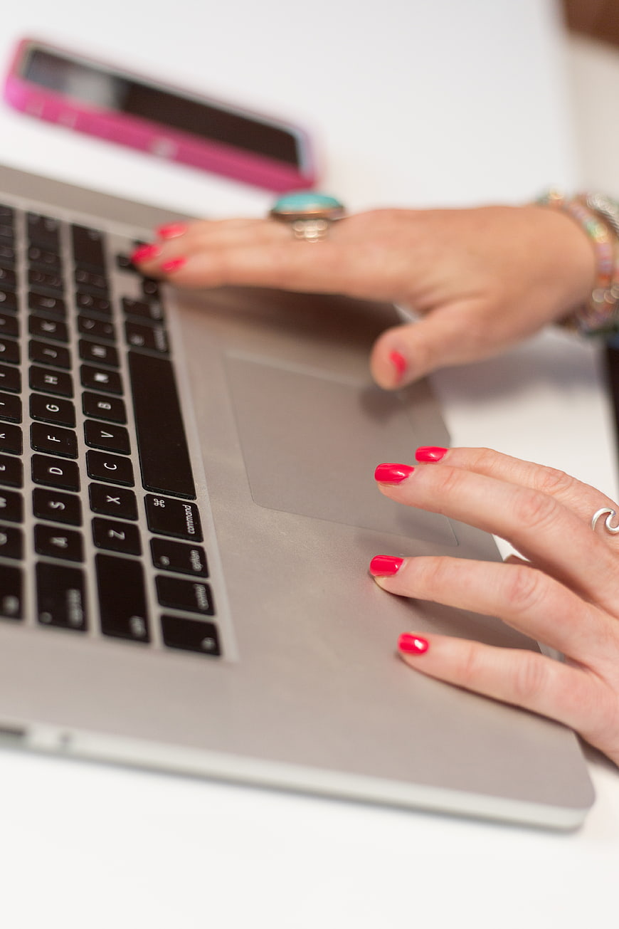 Close-up of woman's hands typing on laptop with red nails