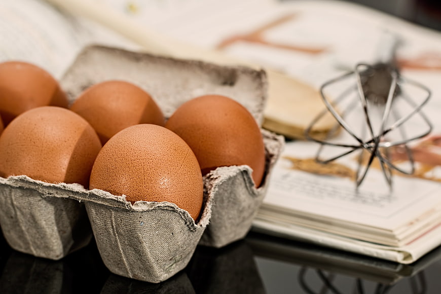 Brown eggs in carton with whisk and cookbook