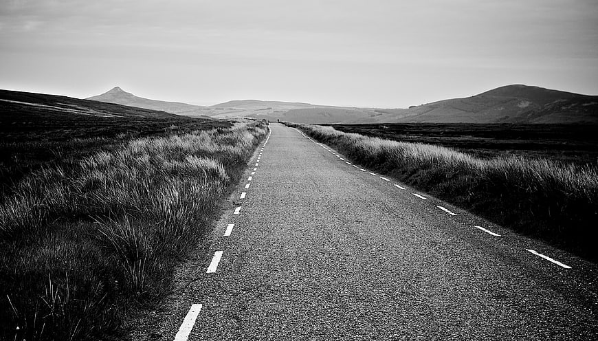 Empty black and white road leading to distant mountains