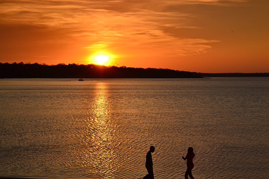 Silhouette of couple walking by lake at golden sunset