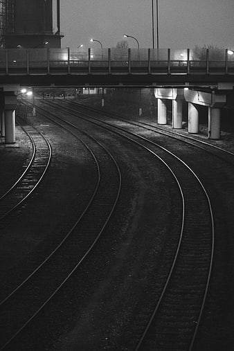 Curved railroad tracks under bridge at night black and white