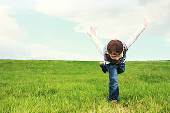 Happy Boy Jumping in Green Meadow with Arms Raised