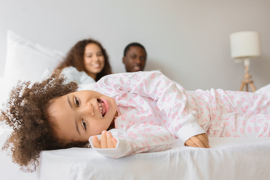 Happy little girl in pajamas lying on bed with parents