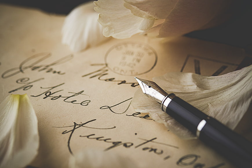 Vintage fountain pen on handwritten letter with white flower petals