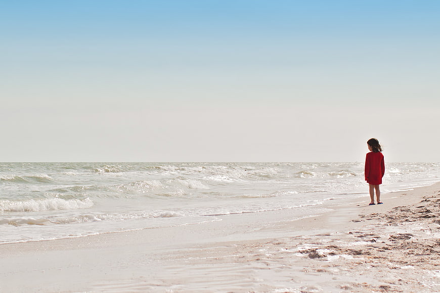 Little Girl in Red Coat Standing Alone on Sandy Beach