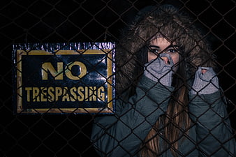 Woman behind chain-link fence with no trespassing sign