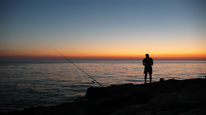 Silhouette of Man Fishing at Sunset on Ocean