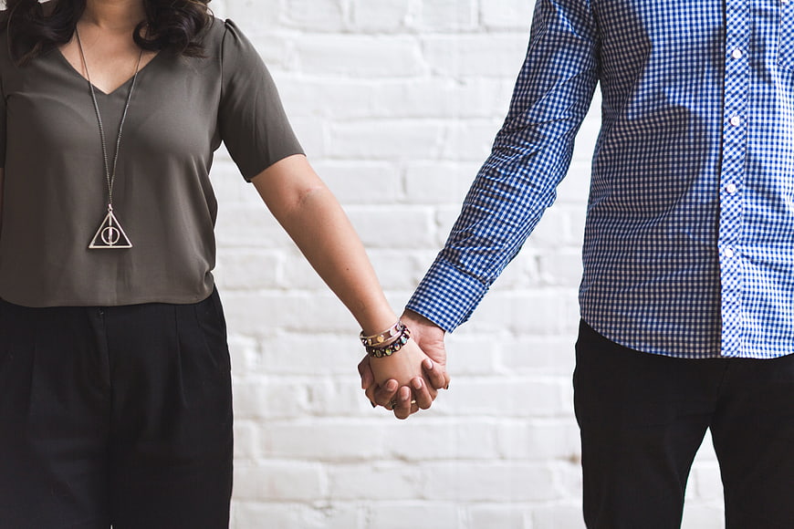 Couple Holding Hands Against White Brick Wall