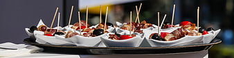 Catering tray of bacon wrapped appetizers with olives and tomatoes