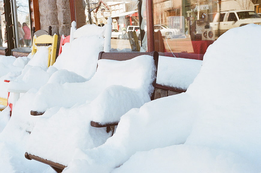Snow-covered wooden chairs outside a storefront window in winter