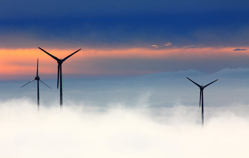 Wind turbines silhouetted against sunset sky above clouds