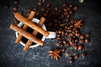 Cinnamon sticks on coffee cup with scattered beans and star anise