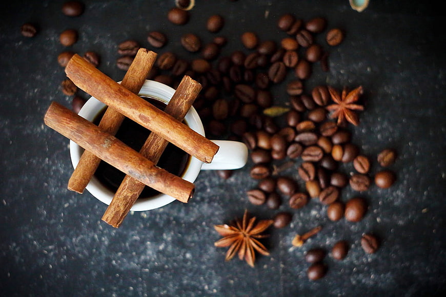 Cinnamon sticks on coffee cup with scattered beans and star anise