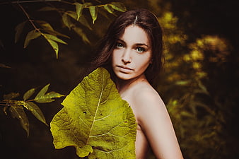 Young woman portrait holding a large green leaf in a dark forest