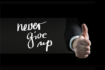 Hand giving thumbs up with never give up text on blackboard