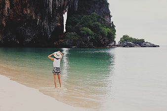 Woman in Hat Standing on Tropical Beach with Limestone Cliffs