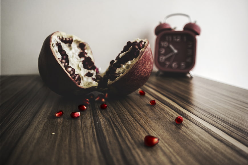 Split pomegranate with scattered seeds on wooden table