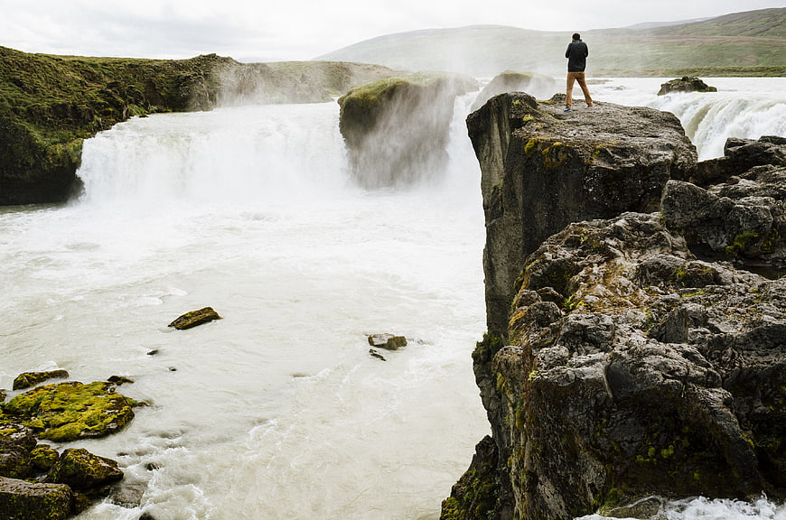 Man standing on cliff edge overlooking powerful waterfall