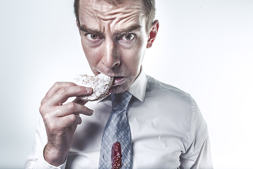 Messy businessman eating donut with intense expression