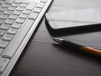 Close-up of white keyboard, smartphone, and pen on dark desk