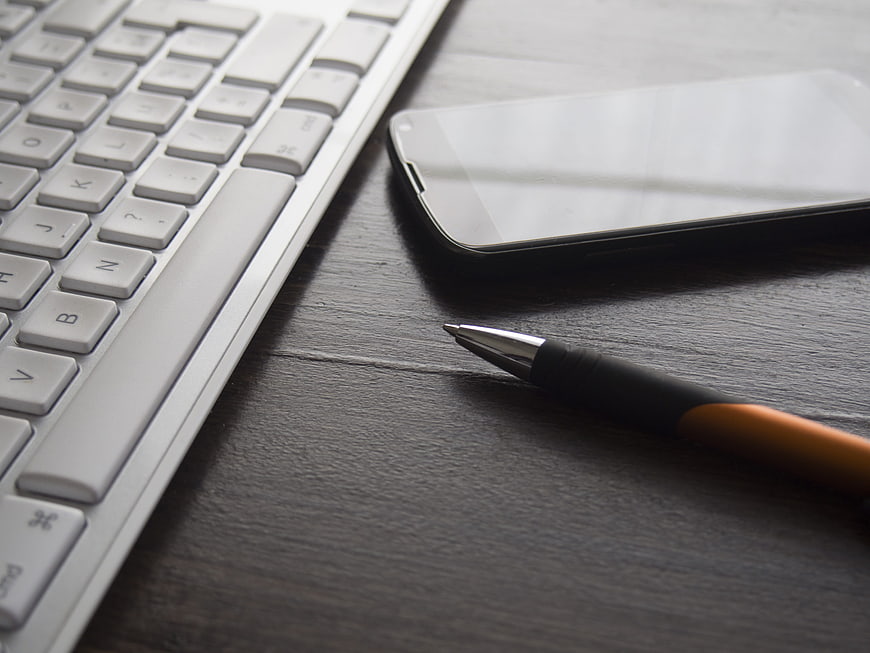 Close-up of white keyboard, smartphone, and pen on dark desk