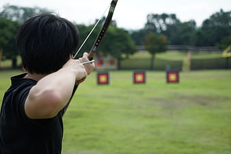 Archer Drawing Bow At Outdoor Archery Range With Targets