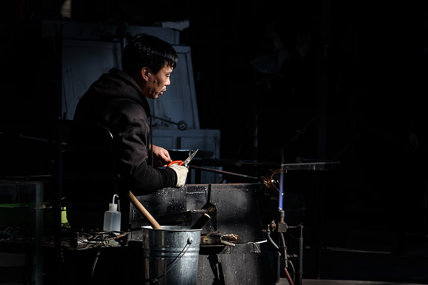 Glassblower working with torch in dark workshop
