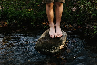 Barefoot child standing on rock in forest stream