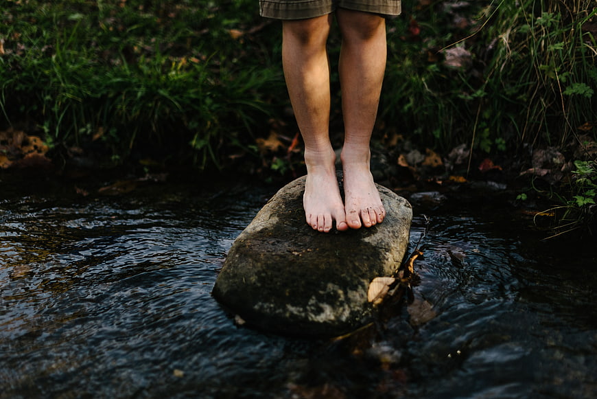 Barefoot child standing on rock in forest stream