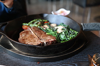 Sizzling T-Bone Steak With Spinach And Vegetables In Cast Iron Skillet