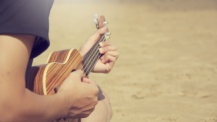 Close-up of hands playing ukulele on sandy beach