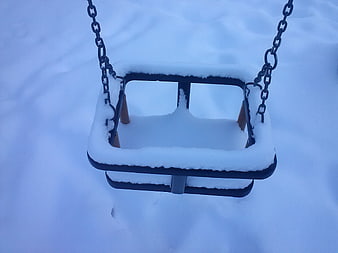 Snow-covered baby swing hanging in a winter park