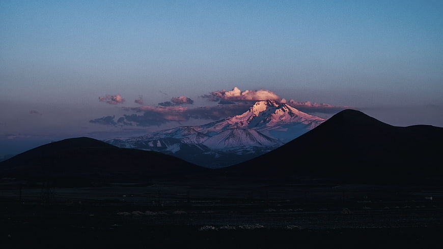 Snow-Capped Mountain Peak at Twilight with Silhouetted Hills