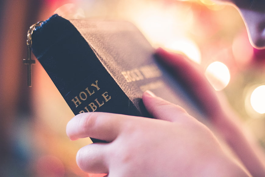 Hands holding Holy Bible with cross bookmark