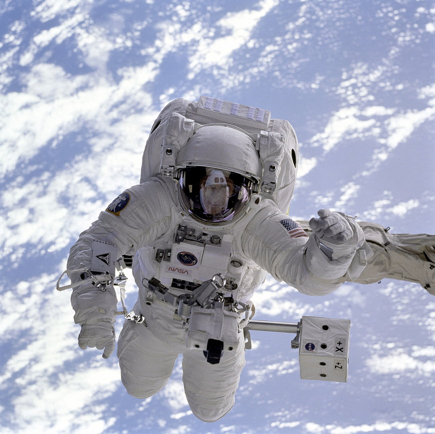 Astronaut performing spacewalk with Earth clouds in background