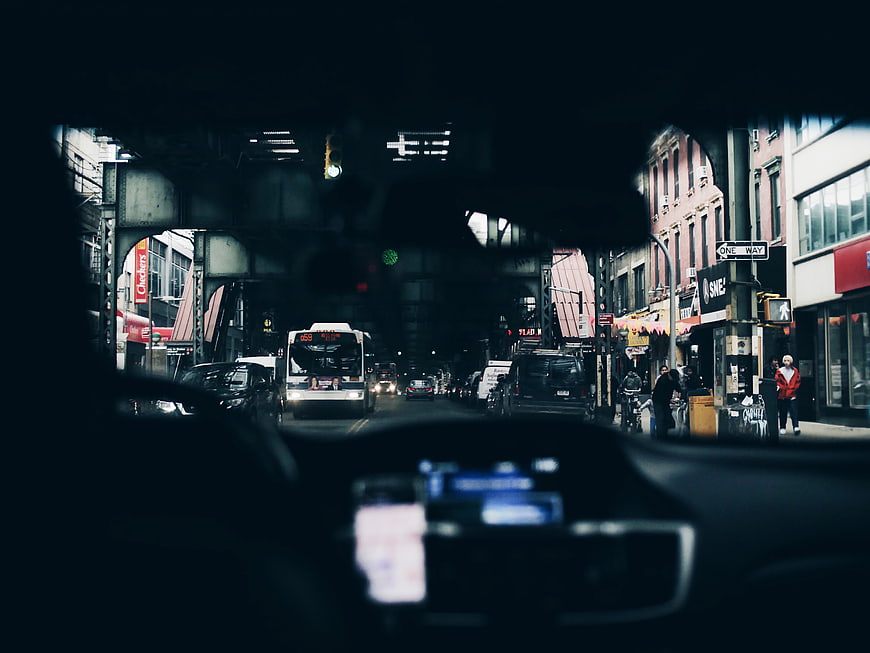 View from car dashboard driving under elevated train tracks in city