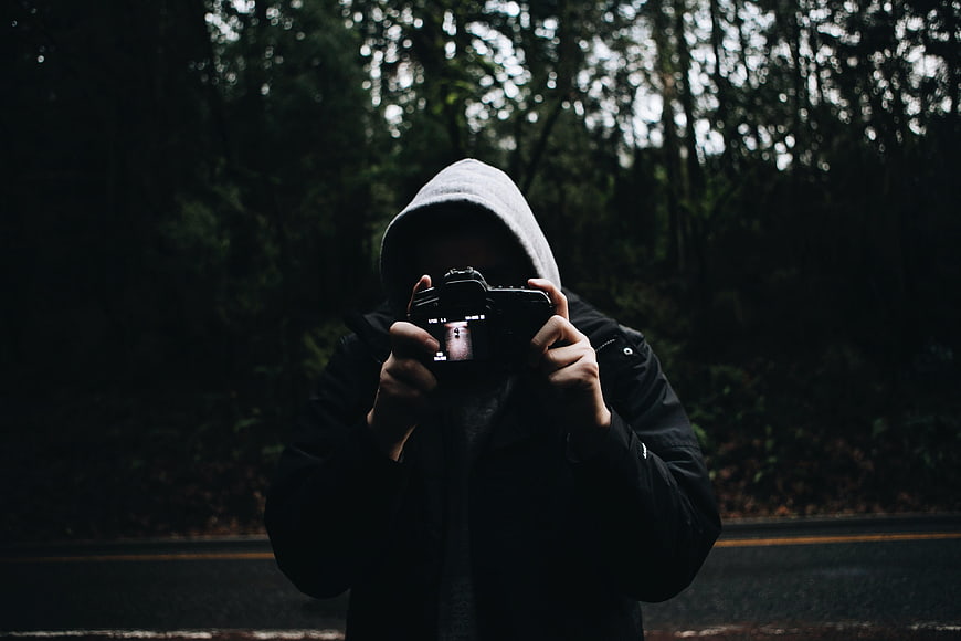 Anonymous Photographer in Hoodie Taking Photo in Dark Forest