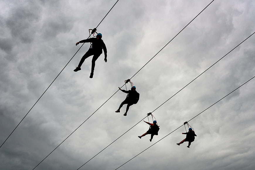 Silhouettes of people zip lining against cloudy sky