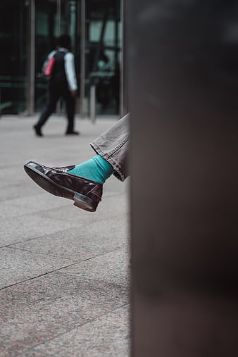 Close-up of brown leather loafer with teal sock on city street