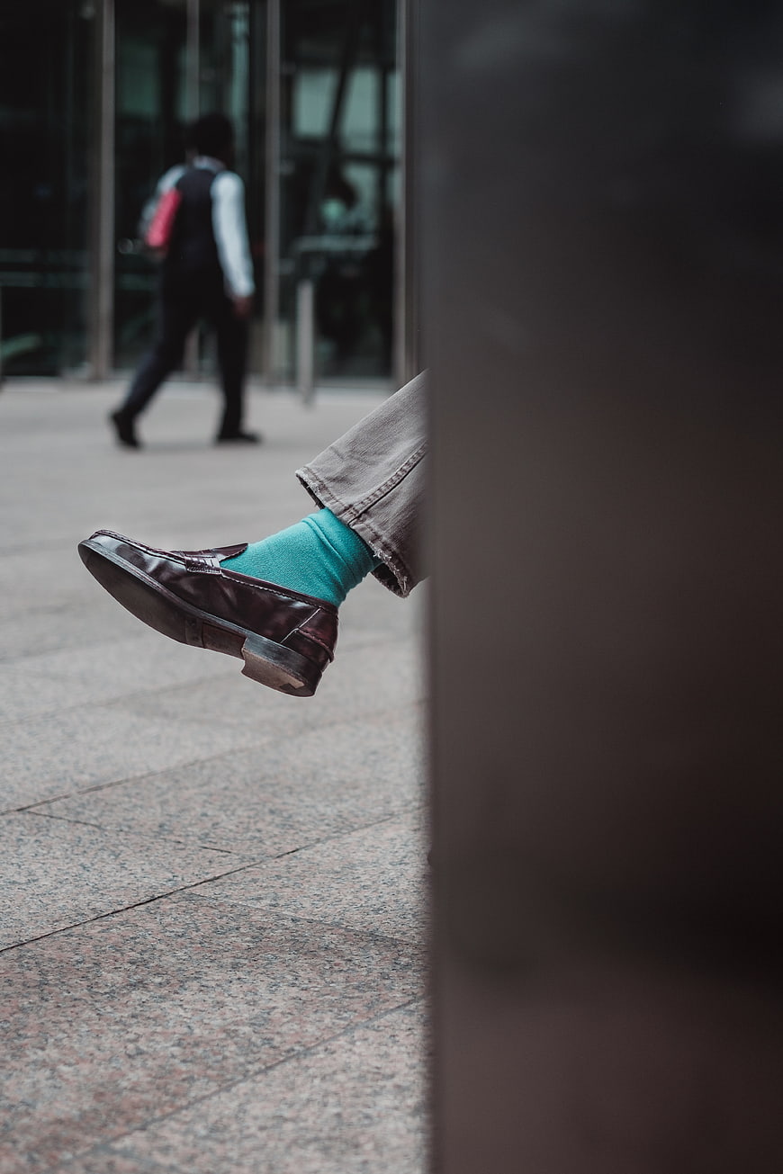 Close-up of brown leather loafer with teal sock on city street