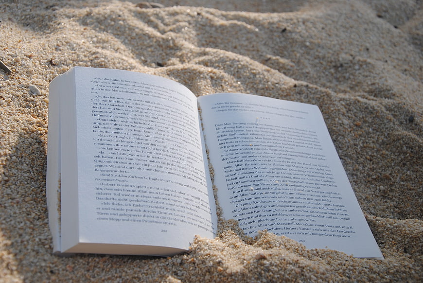 Open book lying on sandy beach with German text