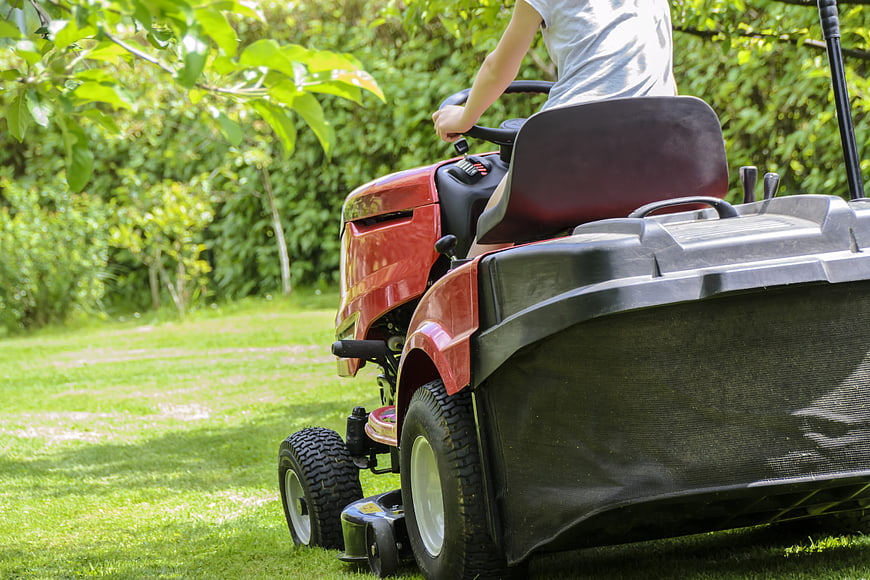 Woman riding red lawnmower tractor in green garden