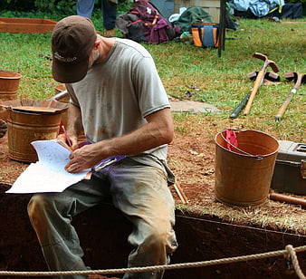 Archaeologist documenting findings at outdoor excavation site