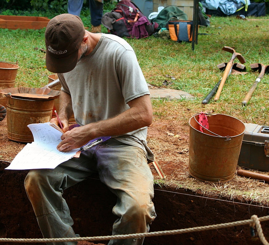 Archaeologist documenting findings at outdoor excavation site