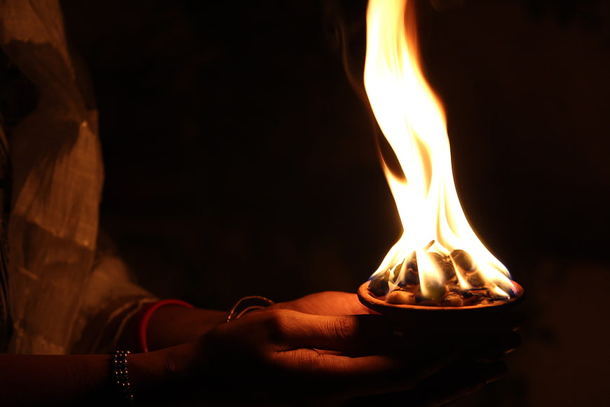 Hands holding traditional clay diya lamp with flame