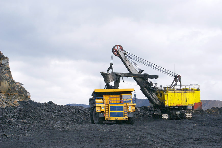 Yellow mining excavator loading coal into dump truck