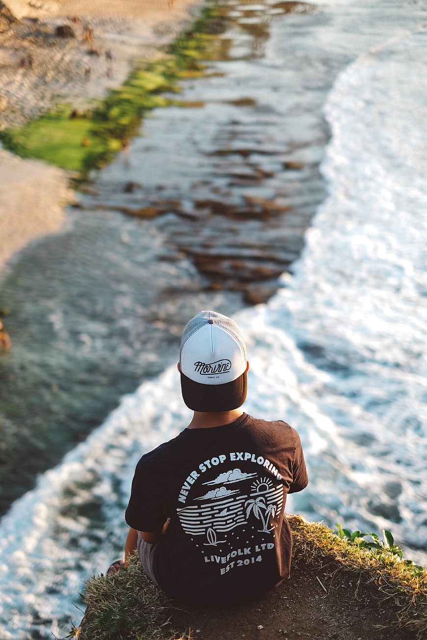Man sitting on cliff overlooking ocean waves at sunset