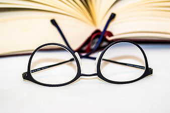 Black reading glasses on white surface with open book